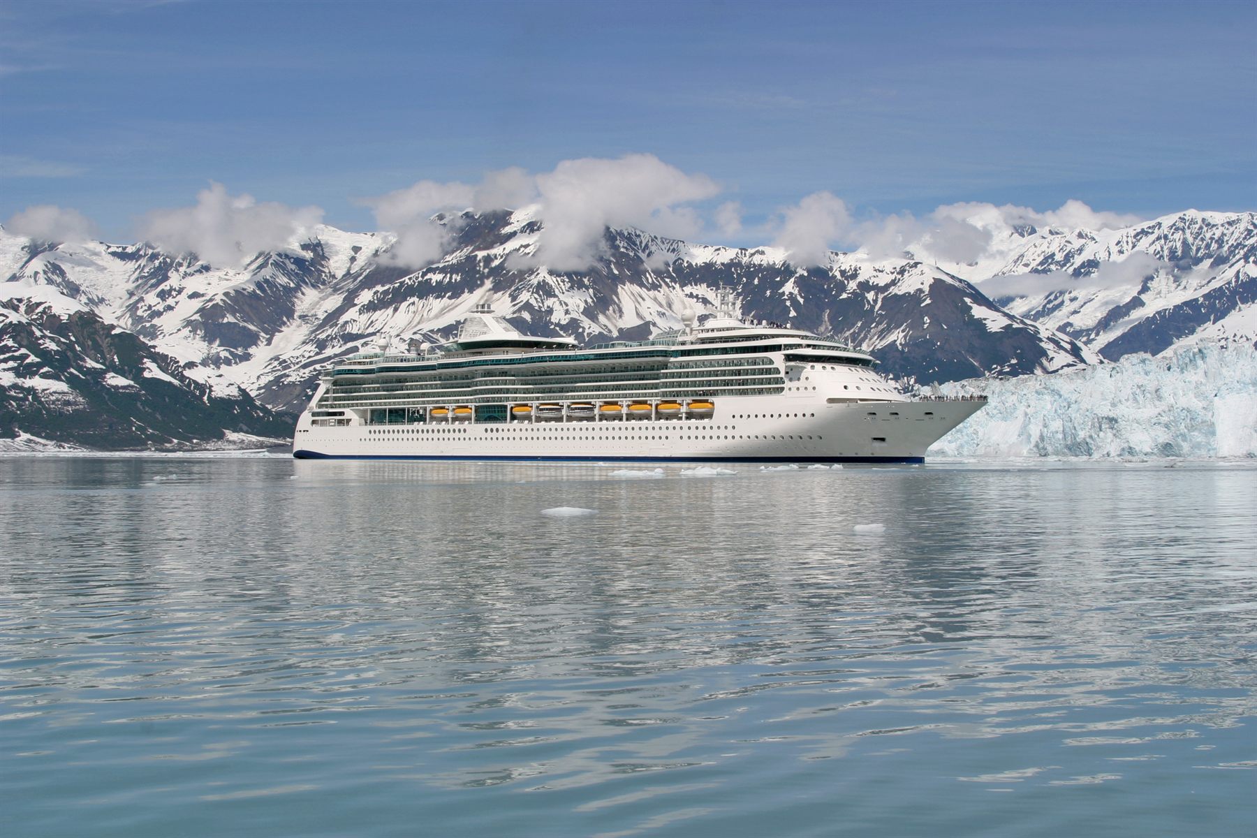 A cruise ship in a glacier-fed fjord below snow-capped mountains