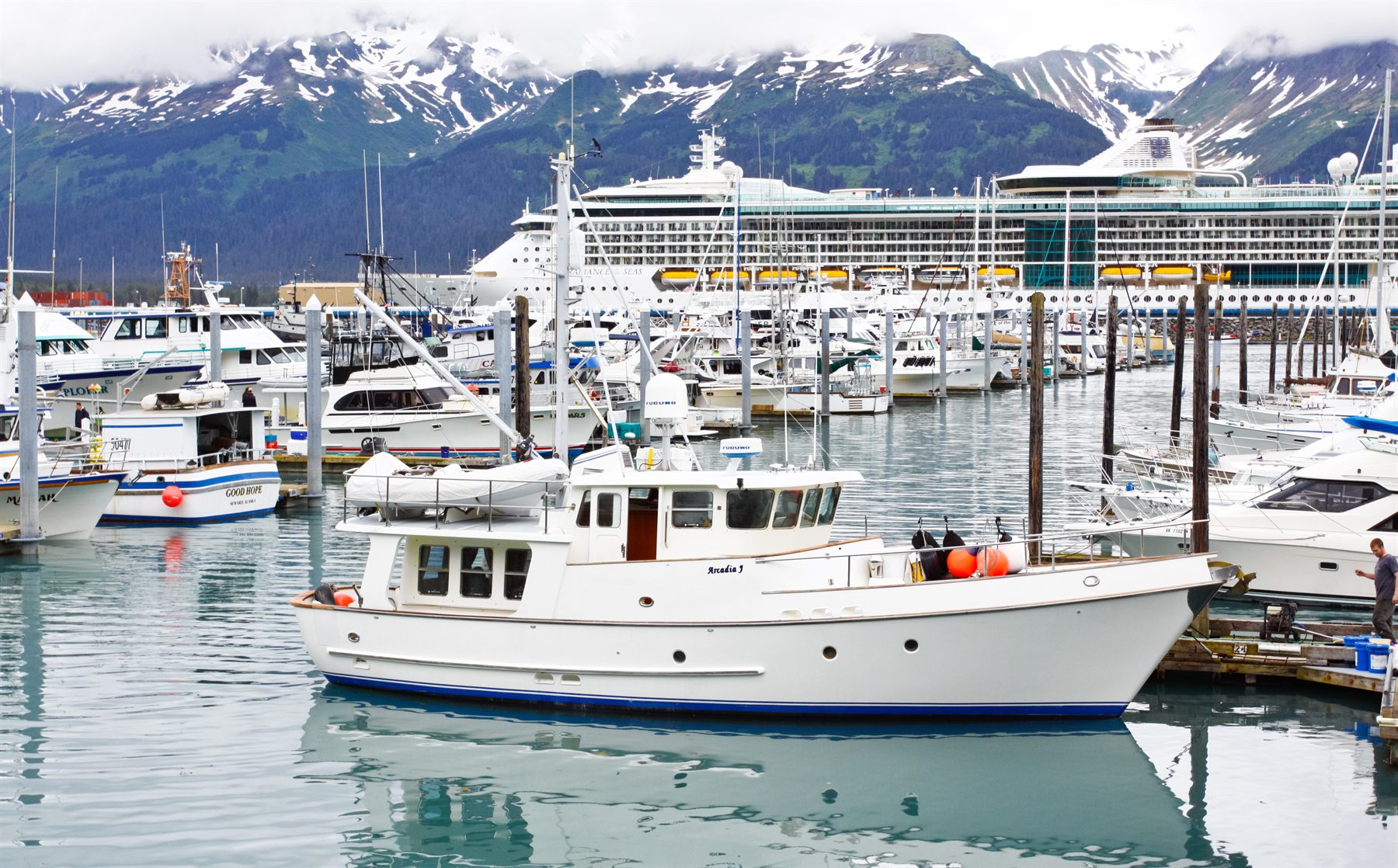 Fishing and pleasure boats in a small harbor with a cruise ship and snowy peaks beyond